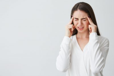 Young beautiful brunette businesswoman holding fingers on temples frowning from pain over white background. Headache. Copy space.